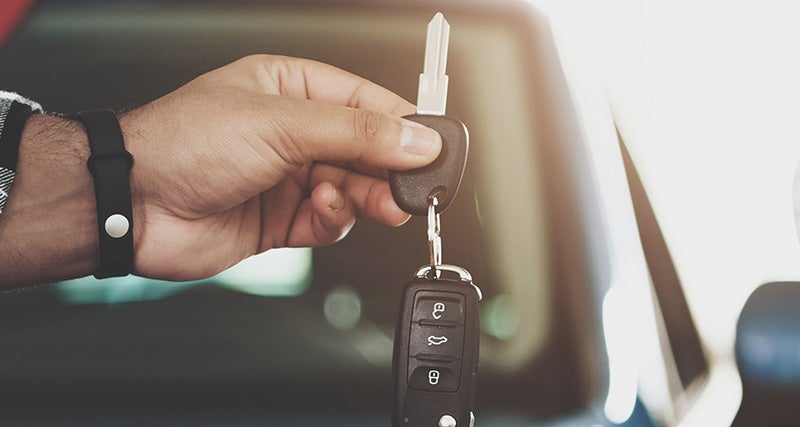 A hand holds a single car key attached to a black car remote.