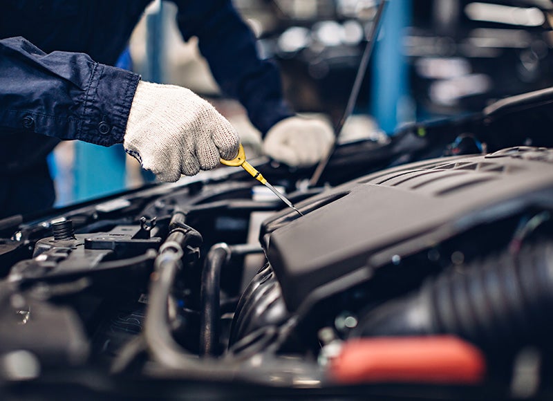 Mechanic in work gloves checking the oil level with a dipstick in a car engine.
